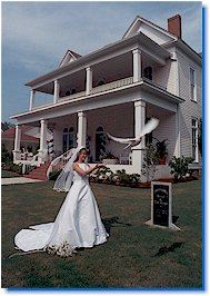 A woman in a wedding dress releasing a dove in front of a white house.